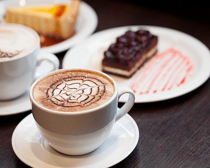 A close up of a cup of Cappuccino and a cake.