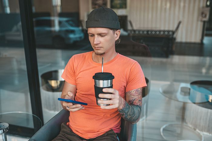 Man in orange t-shirt drinking coffee from reusable coffee cup